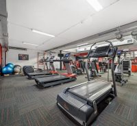 Fitness centrum s běžeckými pásy a cvičebními pomůckami v obchodních prostorech.