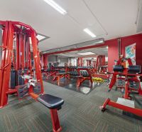 Fitness centrum s červenými posilovacími stroji a činkami, obchodní prostory.
