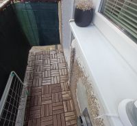 Balkon v 2-pokojovém bytě s podlahou s dřevěným dekorem a květináčem.