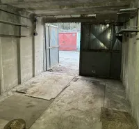 Betonová garáž s otevřenými ocelovými dveřmi, pohled na další garáž venku.