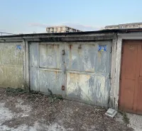 Opuštěné garáže v Bratislavě - Novém Městě s opadanou omítkou a plechovými dveřmi.