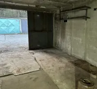 Interiér garáže s betonovou podlahou a kovovými regály.