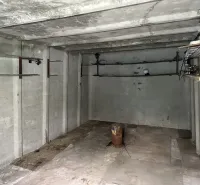 Prázdná betonová místnost s trubkami a osvětlením, interiér garáže.
