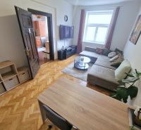Obývací pokoj ve 3-pokojovém bytě disponuje pohodlnou sedací soupravou a podlahou s dřevěným dekorem.