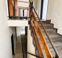 Schodiště v rodinném domě s dřevěným zábradlím a kobercem na schodech.