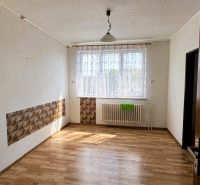 Pokoj v rodinném domě s podlahou s dřevěným dekorem, závěsem a radiátorem pod oknem.