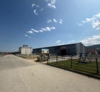 Průmyslová budova v Hniezdnem s jasně modrou oblohou a příjezdovou cestou.