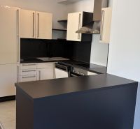 Kuchyně v 3-pokojovém bytě s elegantní černou deskou a světlými skříňkami.