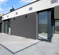 Prostorná terasa 5 a více pokojového bytu s moderní fasádou a skleněným zábradlím.