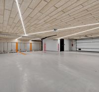 Parkovací garáž s betonovým stropem a podlahou, osvětlená lineárními svítidly.