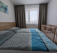Světlá ložnice s postelí a dětskou postýlkou ve 2pokojovém bytě.