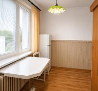 Kuchyně v 2-pokojovém bytě se stolem, židlí, lednicí a podlahou s dřevěným dekorem.