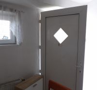 Vchodové dveře v 2-pokojovém bytě s dřevěným dekorem komody a židle.