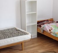 Dvě postele, polička a podlaha s dřevěným dekorem v 2-pokojovém bytě.
