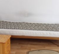 Postel v pokoji s podlahou s dřevěným dekorem, vedle dřevěná skříňka.