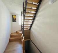 Schodiště s dřevěným dekorem v rodinném domě se světlým interiérem a obrazem na stěně.