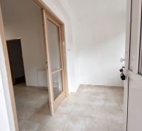 Vchod se světlými dlaždicemi a prosklenými dveřmi v rodinném domě.