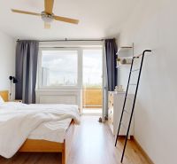 Světlá ložnice s postelí, ventilátorem, podlahou s dřevěným dekorem a přístupem na balkon ve 3pokojovém bytě.