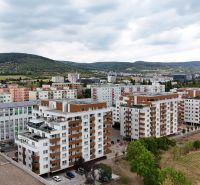 Pohled na bytové domy na Nobelově ulici, Bratislava - Nové Město, obklopené zelení a kopci.