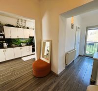 Interiér s kuchyňskou linkou, podlahou s dřevěným dekorem a balkónovými dveřmi ve 2-pokojovém bytě.