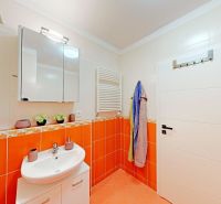 Koupelna v 2-pokojovém bytě se světlou sanitou a oranžovými obklady.