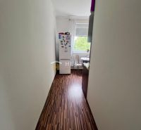 Úzká chodba s podlahou s dřevěným dekorem vede do kuchyně v 2-pokojovém bytě.