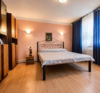 Ložnice s kovovou postelí, podlaha s dřevěným dekorem, nábytek a závěsy v rodinném domě.