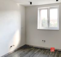 Jednoduchý pokoj v jednopokojovém bytě s podlahou s dřevěným dekorem a bílými stěnami.