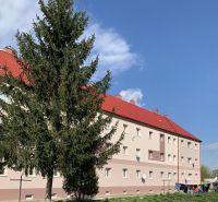 Budova s červenými střechami a před ní strom, na Železniční ulici v Šahách.