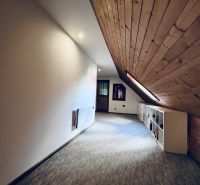 Podkrovní chodba v rodinném domě s dřevěným stropem a nízkými skříňkami.