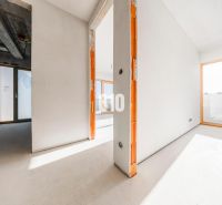 Prostorný interiér nedokončeného 3-pokojového bytu s velkými okny a betonovým stropem.