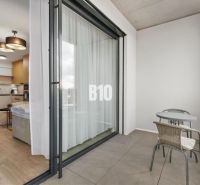 Balkon s posezením a výhledem do 1-pokojového bytu přes posuvné dveře.
