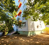 Bytovka s barevnými balkóny na ulici Lúky ve Vráblech, obklopená stromy.