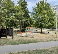Dětské hřiště obklopené stromy v parku města Topoľčany blízko 1-pokojového bytu.