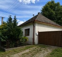 Rodinný dům v Urmincích na ulici Klačany, obklopený dřevinami a plotem.
