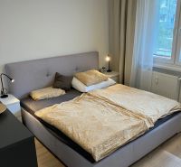 Ložnice s velkou postelí, nočními stolky a podlahou s dřevěným dekorem ve 3pokojovém bytě.