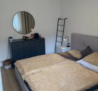 Ložnice s postelí, komodou a kulatým zrcadlem v 3-pokojovém bytě.