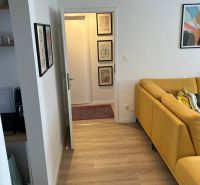 Světlá podlaha s dřevěným dekorem a žlutá pohovka v 3-pokojovém bytě.