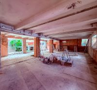 Nedokončené obchodní prostory s betonovou podlahou, žebříky a stavebním materiálem.