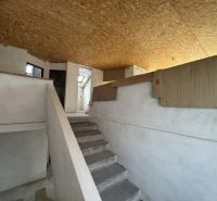 Interiér rodinného domu se schodištěm, bílými stěnami a OSB deskami na stropě.