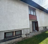 Rodinný dům v Plavnici se světlou omítkou a dřevěnými okny v přízemí.