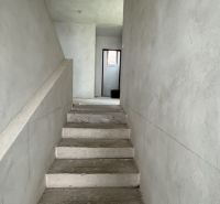 Betonové schody vedoucí do patra v rodinném domě s omítnutými stěnami.