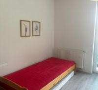 Garsonka s postelí, červenou přikrývkou a podlahou s dřevěným dekorem.