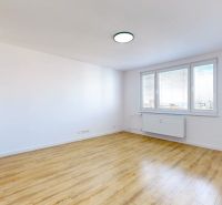 Prostorný pokoj s velkými okny a podlahou s dřevěným dekorem v 3-pokojovém bytě.
