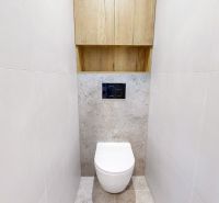 Toaleta se stěnami z bílých dlaždic ve 3pokojovém bytě, se skříňkou nad WC.