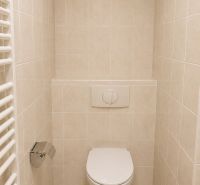 Koupelnové WC ve 2pokojovém bytě s dlažbou a nástěnným splachovacím zařízením.
