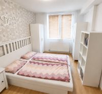 Světlá ložnice s manželskou postelí, květinovou tapetou a podlahou s dřevěným dekorem.