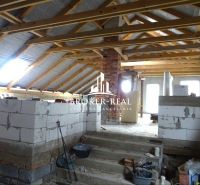 Rozestavěný podkrovní prostor v rodinném domě, s viditelnými dřevěnými trámy a stavebním materiálem.