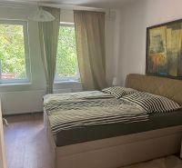 Ložnice ve 3pokojovém bytě s postelí, podlahou s dřevěným dekorem a obrazem na stěně.