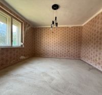 Pokoj v rodinném domě s květinovou tapetou a velkými okny.